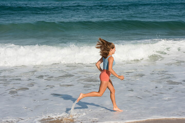 Pretty athletic young woman in shorts and crop top running on the sunny beach