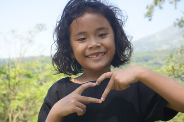 little girl with curly hair smiling with her fingers making a love sign as a symbol of love and peace