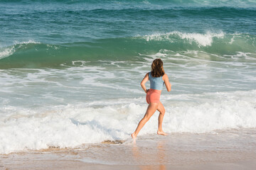 Pretty athletic young woman in shorts and crop top running on the sunny beach