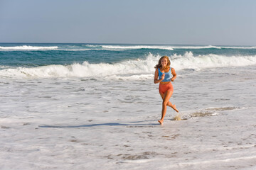 Pretty athletic young woman in shorts and crop top running on the sunny beach