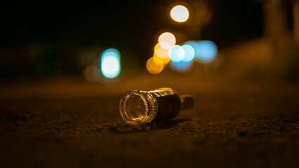 Selective focus shot of empty bottle of alcohol thrown in the middle of street on bokeh background