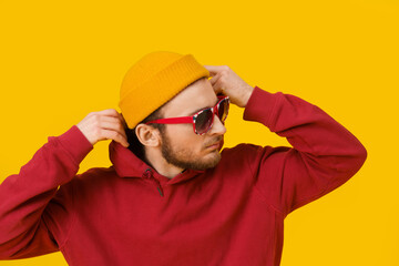 Close up portrait of pensive young man in casual wear in sunglasses posing sideways on yellow...