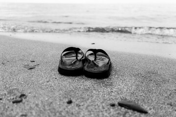 Closeup grayscale shot of slippers on the beach