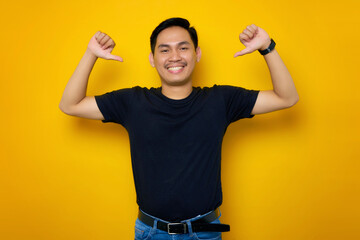 Cheerful young Asian man in casual t-shirt pointing at herself with proud isolated on yellow background. People lifestyle concept