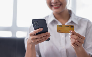 Cropped shot smiling young Asian woman using a credit card and shopping online payment on smartphone at home.
