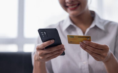 Cropped shot smiling young Asian woman using a credit card and shopping online payment on smartphone at home.