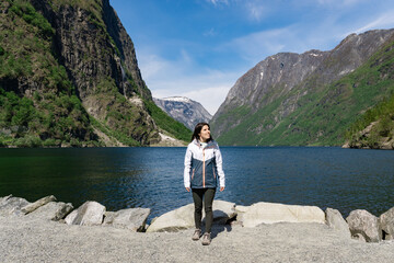 Fototapeta na wymiar Young tourist girl at the foot of the fjord surrounded by high mountains in Gudvangen - Norway