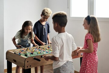 Group of multi-cultural cute children spending playtime with friends playing foosball together.