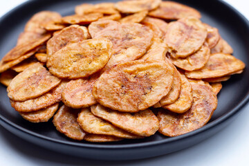 Banana chips in black plate on white background