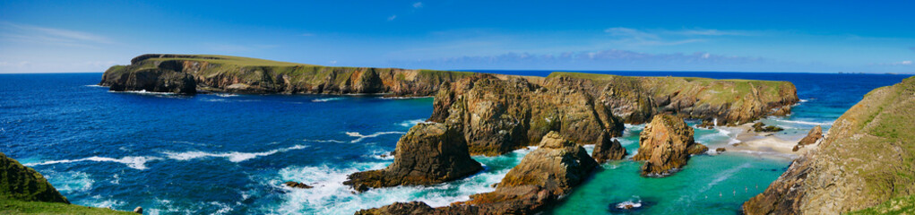 Fototapeta na wymiar A panorams of the rugged coastal cliff scenery and pristine turquoise waters around the island of Uyea in Northmavine, Shetland, UK. Taken on a sunny day with a blue sky.