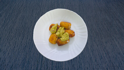 croquettes with guacamole sauce in white plate on dark blue tablecloth