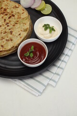 Famous punjabi Indian food Aloo paratha or potato stuffed flat bread. served with tomato ketchup on white background, popular north Indian Punjabi food dish on white background in brown dish plate