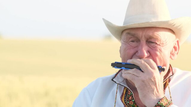 Close-up of the face of an old man in a hat playing the harmonica. 