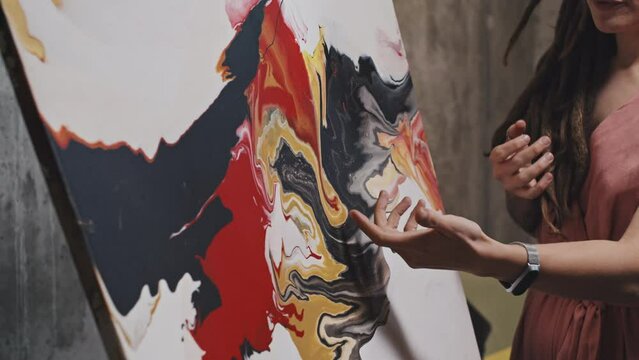 Midsection of cropped Caucasian woman with dreadlocks presenting modern abstract painting, speaking in art gallery