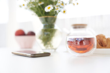 Top view of a tea with fresh sweet croissants on the table with a vase of daisies. In the middle of the table is a smartphone. Sunday breakfast in backyard of a cottage. Copy space. High quality photo