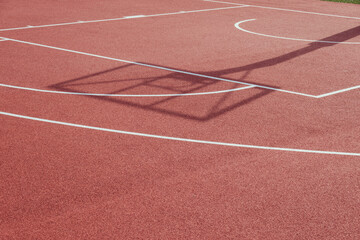 Shadow of the rack with shield and basketball ring on orange basketball rubber field ground during sunny day outdoors. Basketball game background