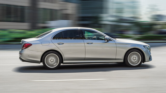 Mercedes E Class on the road in motion. Fast speed drive on city road. Side view of moving silver car on the street