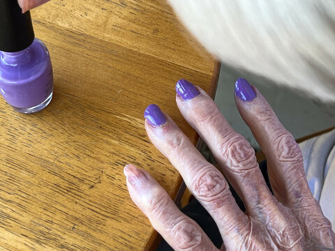 Senior woman polishing her nails with purple nail polish and giving herself a manicure.