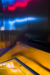 Vertical shot of a modern stair handrail hallway with metal walls reflecting colorful lights