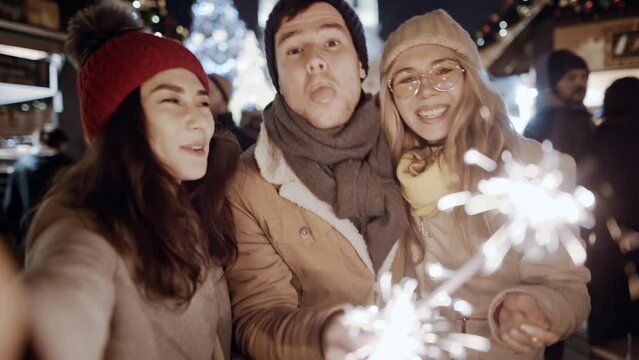Beauty young multiracial friends asian girl use smartphone communicating, podcast video chat Europe night street. Woman looking at phone selfy with falling sparkling glowing sparklers fireworks light.