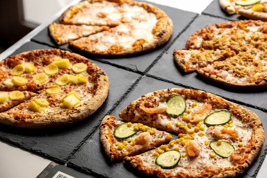 Spread Of Four Types Of Pizzas Set On Black Stone Plates