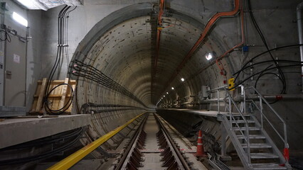 Concrete tunnel with railroad and electricity cables, metal staircase and lights