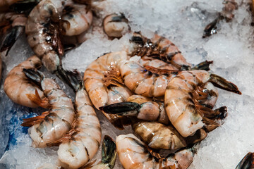 A pile of large pink shrimp sitting on ice at an outdoor farme'r market or fish market