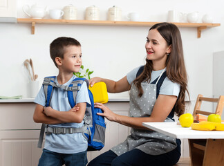 Caring mother puts yellow plastic lunch box to her son in a school backpack. School food or lunch, concept image.