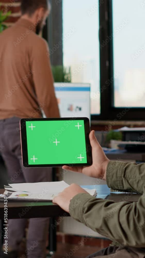 Poster vertical video: company employee looking at tablet with horizontal greenscreen on display, working o