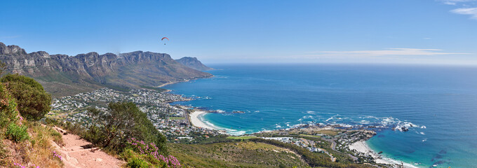 High landscape ocean view of mountains. Clear big blue sky and sea surrounded by nature and life creating peace and tranquility. An outdoor rocky path and waves against the coast around greenery.