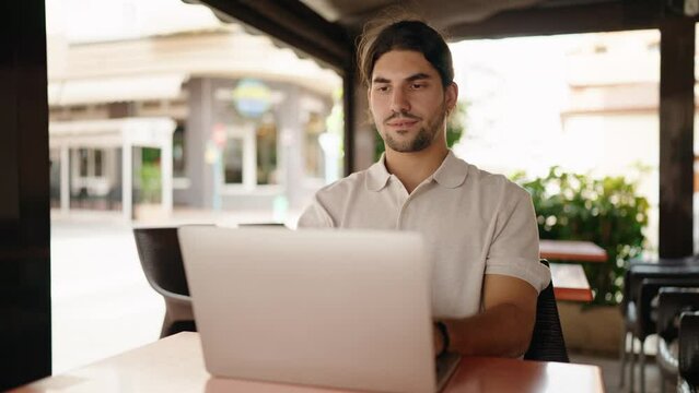 Young hispanic man sitting on table finishing work at coffee shop terrace