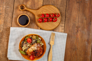 Udon with vegetables and chicken with sesame in a wooden plate on a napkin next to tomatoes and...