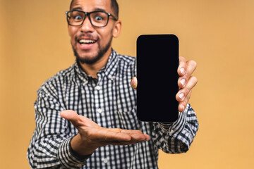 Portrait of a smiling attractive african american black man holding blank screen mobile phone isolated over beige background.