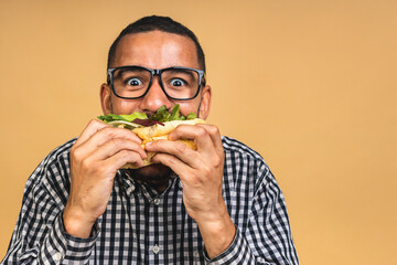 Hungry young african american black man eating hamburger isolated over beige background. Diet or Fast food concept.