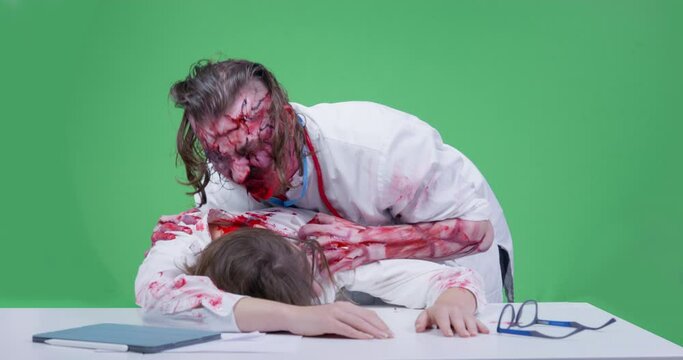 Creepy zombie in medical uniform attacked young woman lying on table, and now bites off pieces of meat that fall out of his mouth, chromakey background. Halloween themed zombie apocalypse party
