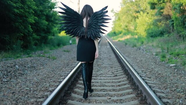 The goddess of death and bloody revenge walks on rails. Fallen black angel with black wings. Halloween concept.