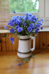 Bouquet of wild blue cornflowers in a vase by the window, blurred floral background