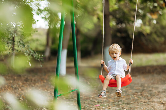 funny toddler boy swings on a swing. Little kid on a walk in the summer park. The concept of children's summer vacation, Family leisure and outdoor play concept. safety on the playground.