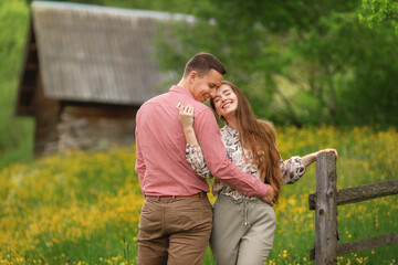 Young loving couple gently hugging on the wood house background, a lot of yellow flowers are around on the field. Enjoying time together.  © Татьяна Яблокова