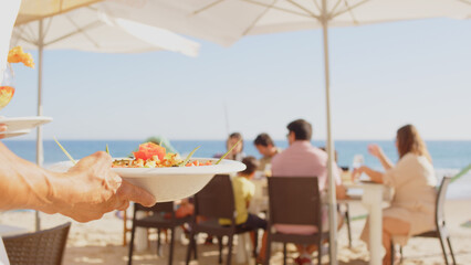 Professional waiter bringing different plates - paella, salad, prawns in tempura - to a family's...