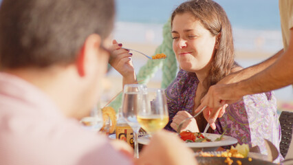 Family and friends gathered for lunch enjoying a delicious paella in a bar on the beach - happy little kids playing around the table after eating, eating dessert and ice cream