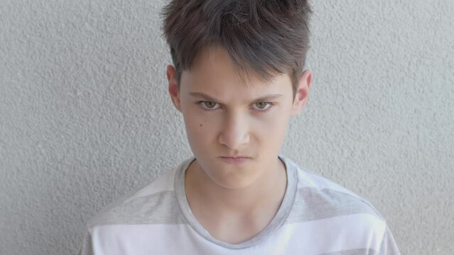 Teenage boy pretend angry, looking direct to camera angrily, but then smile. Funny teenager portrait