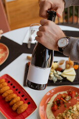 man opens a bottle of wine with a corkscrew over a table with many food and snacks