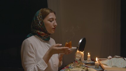 4K. Slavic woman in a headscarf brings a candle to the mirror