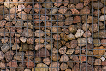 Stones behind metal fence texture background. Decorative hedge with colorful, natural stones. Ecological construction materials. Pile of rocks. Close up, selective focus