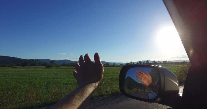 Woman Holding Hand Out Car Window Feeling Wind Blowing Through Fingers Driving In Countryside