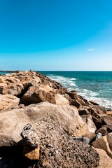 Vertical shot of a rocky shore on the Dana Point under a blue sky - obrazy, fototapety, plakaty