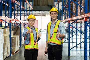 A Man and a Female with yellow helmet and man warehouse worker show thumb up together for successful job with happy face. Team spirit working together in storehouse to complete the balance inventory,