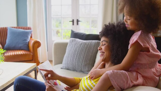 Daughter sitting on back of sofa at home with mother reading book together - shot in slow motion