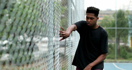 Black guy at basketball court holding into metal fence posing